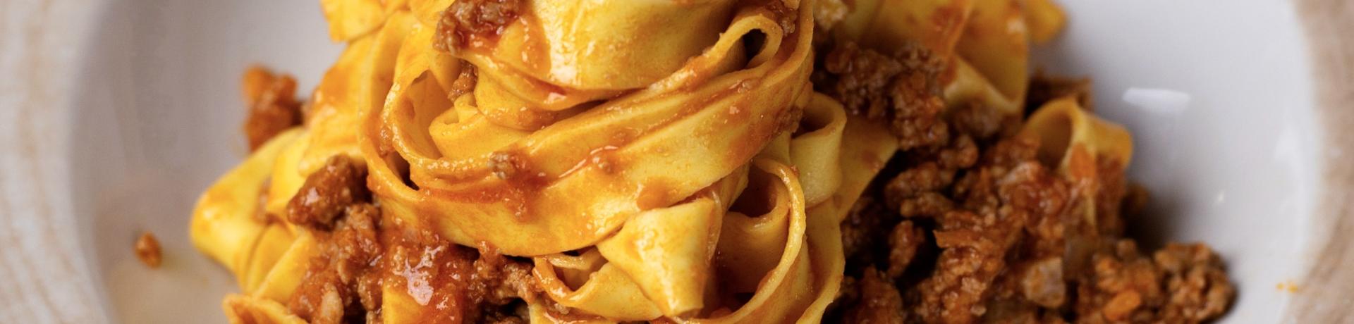 Tagliatelle al ragù servite in un piatto rustico con bordo decorato.
